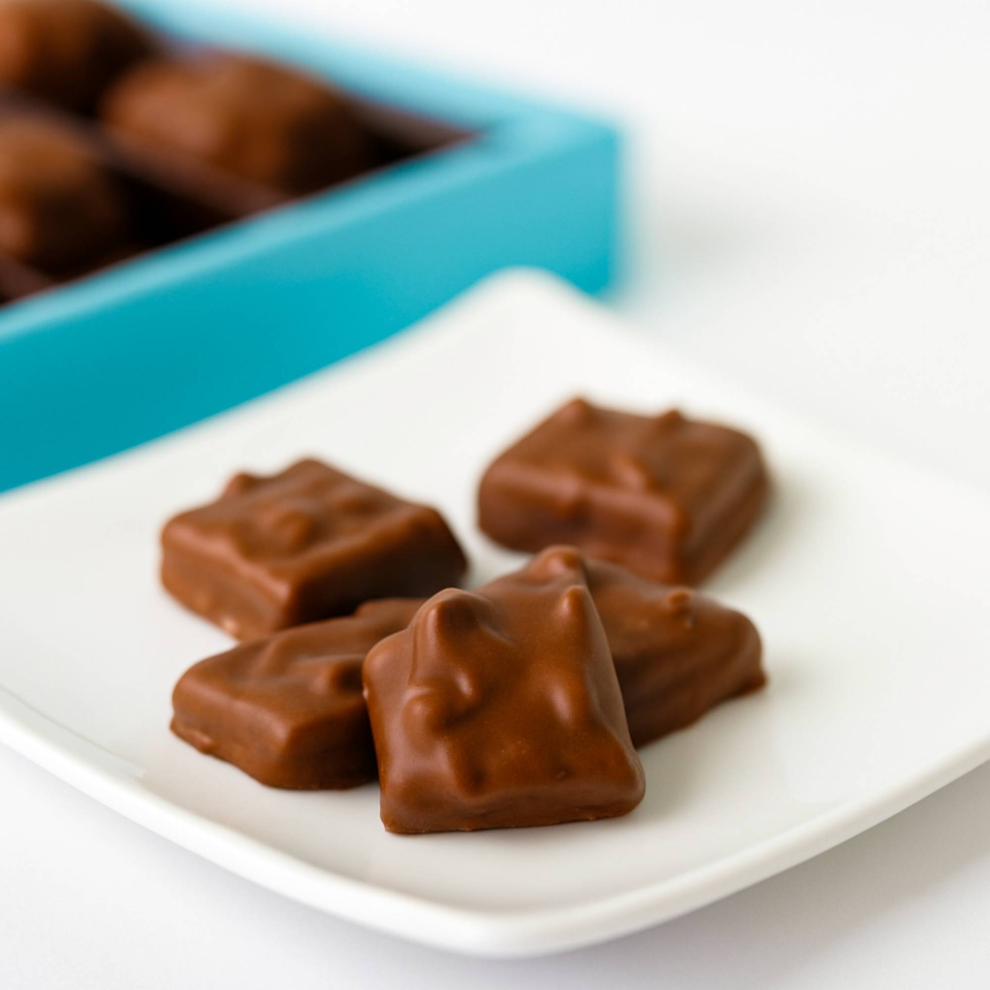 Sugar free milk chocolate toffee with almonds on a white plate and a blue box in the background