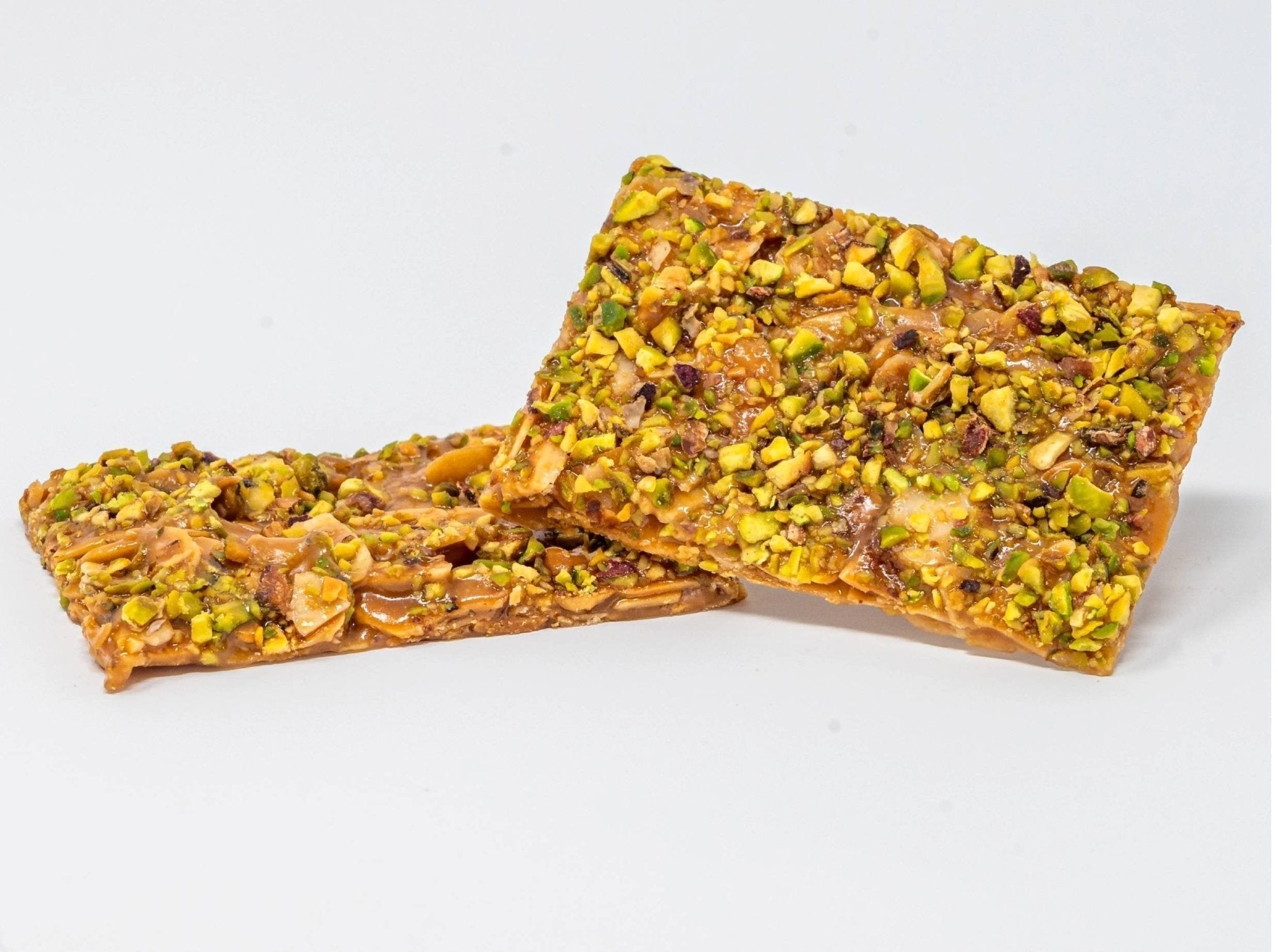 Two pieces of Italian pistachio brittle candy with chopped pistachios on a white background
