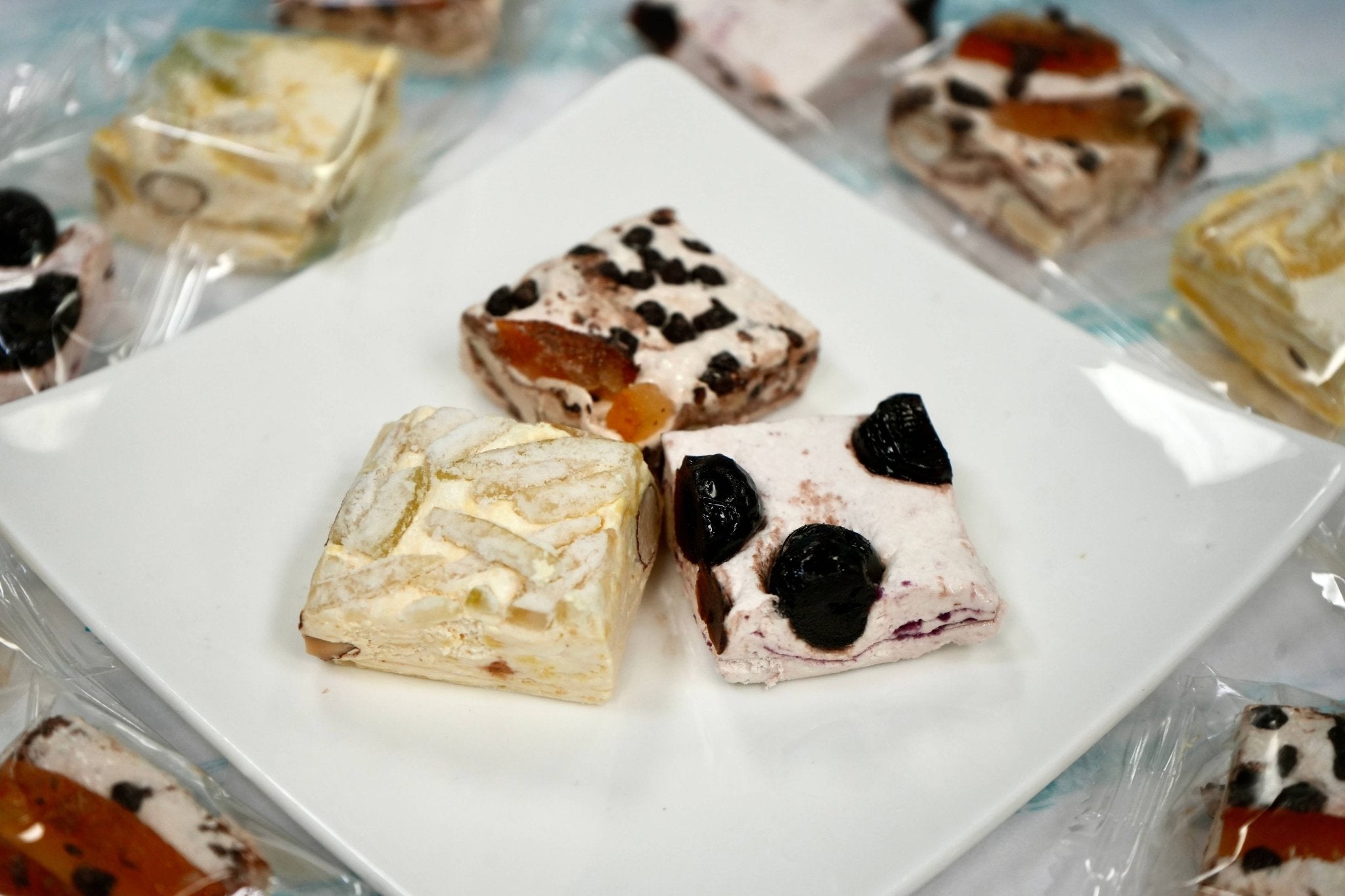 Almond Nougat Turron Candy Gourmet roasted almond soft nougat brittle, cherry, chocolate orange, and lemon confections plated on a white dish. Andy Anand Chocolates, All Products, Products, Soft Brittle Nougat, -Brittle, Brittle / Turron.