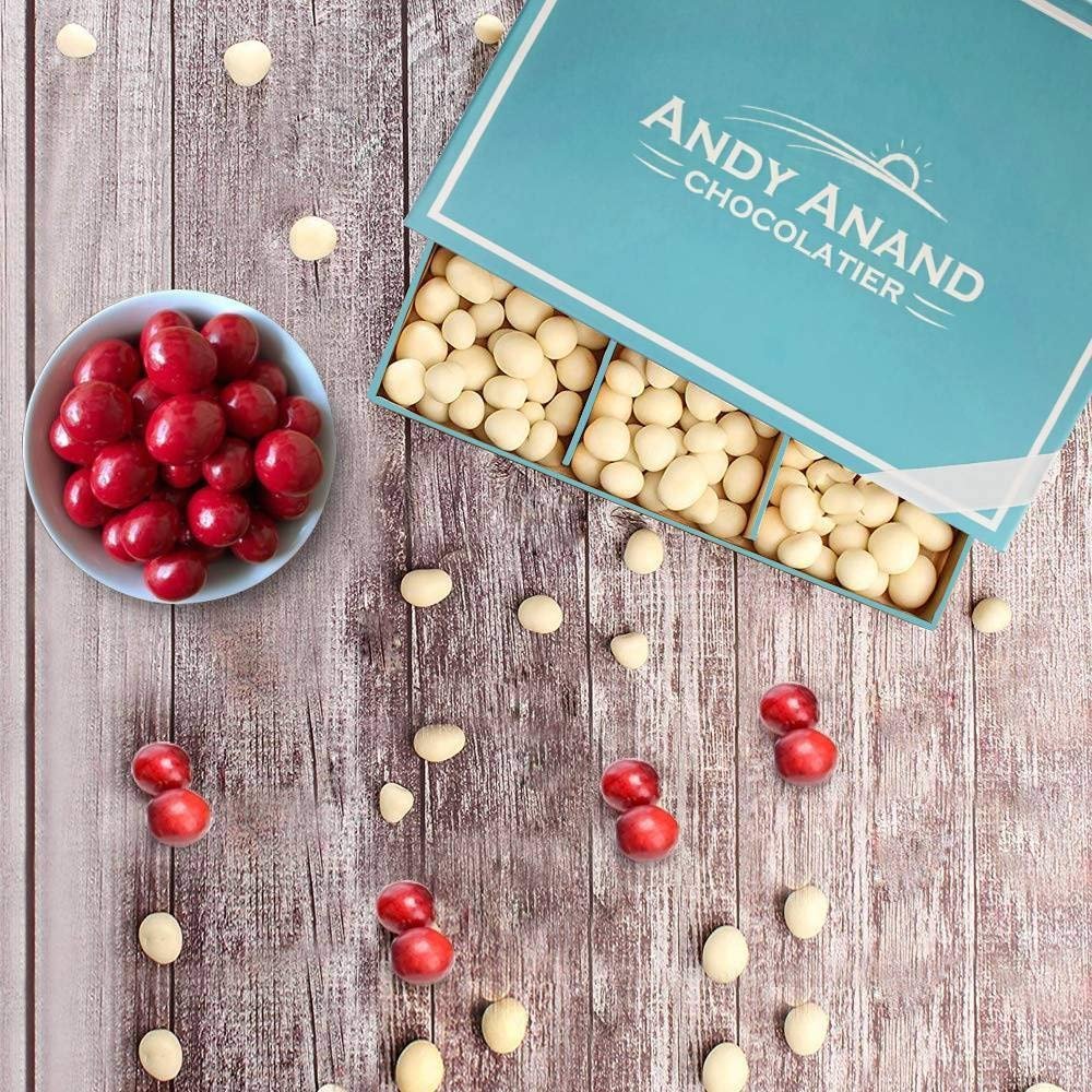 White chocolate covered California cranberries in a blue Andy Anand Chocolatier box and scattered on a wooden surface